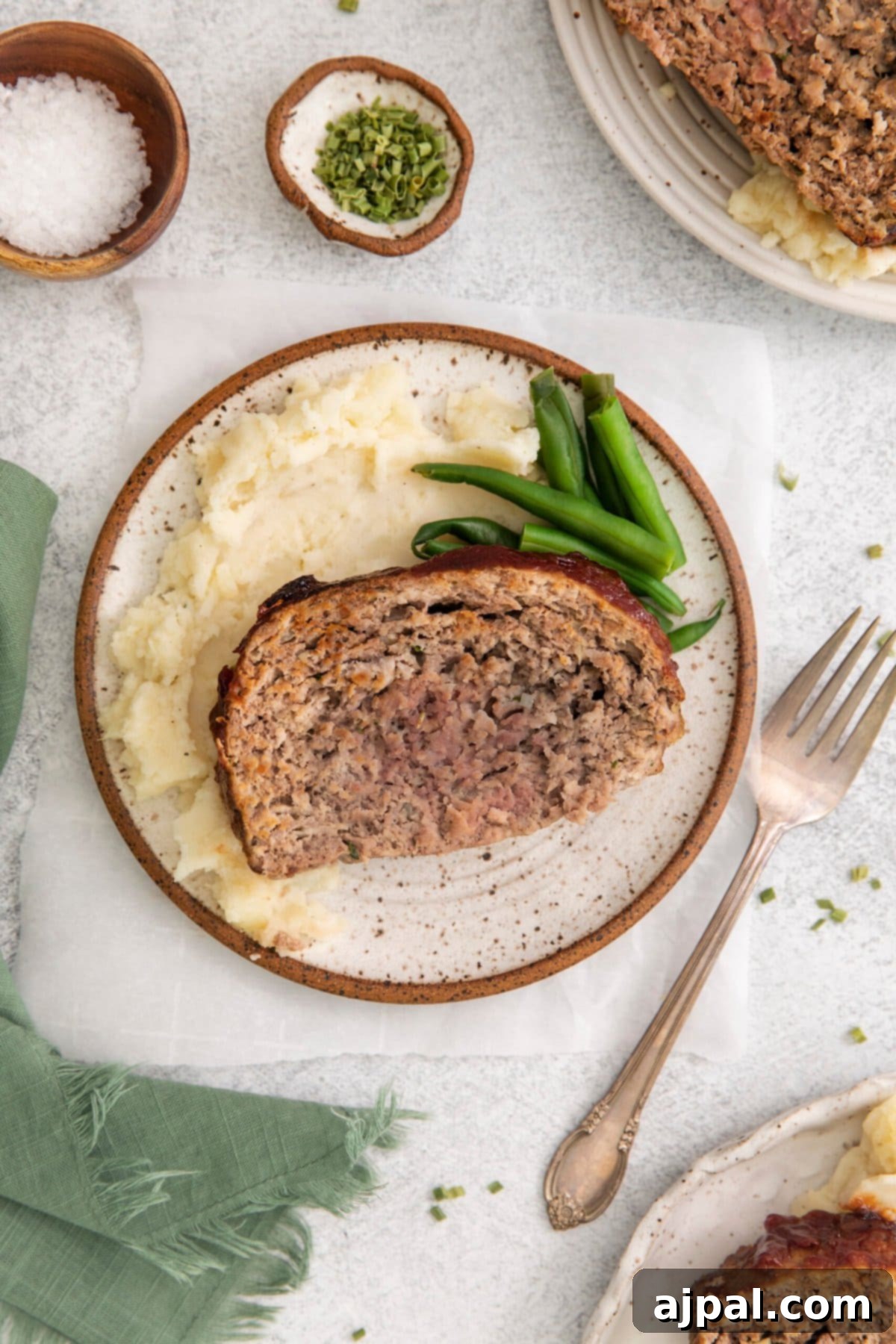 picture of a slice of meatloaf on a white plate on a table next to a fork
