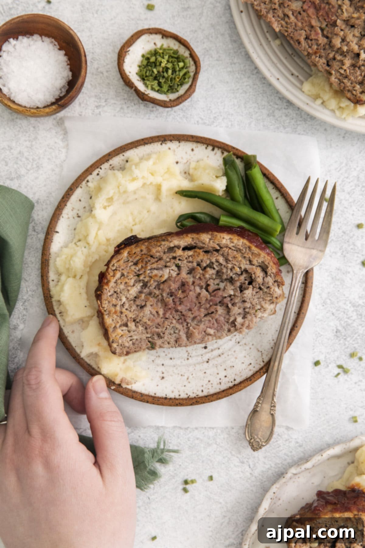 hand touching plate with meatloaf, potatoes, and green beans