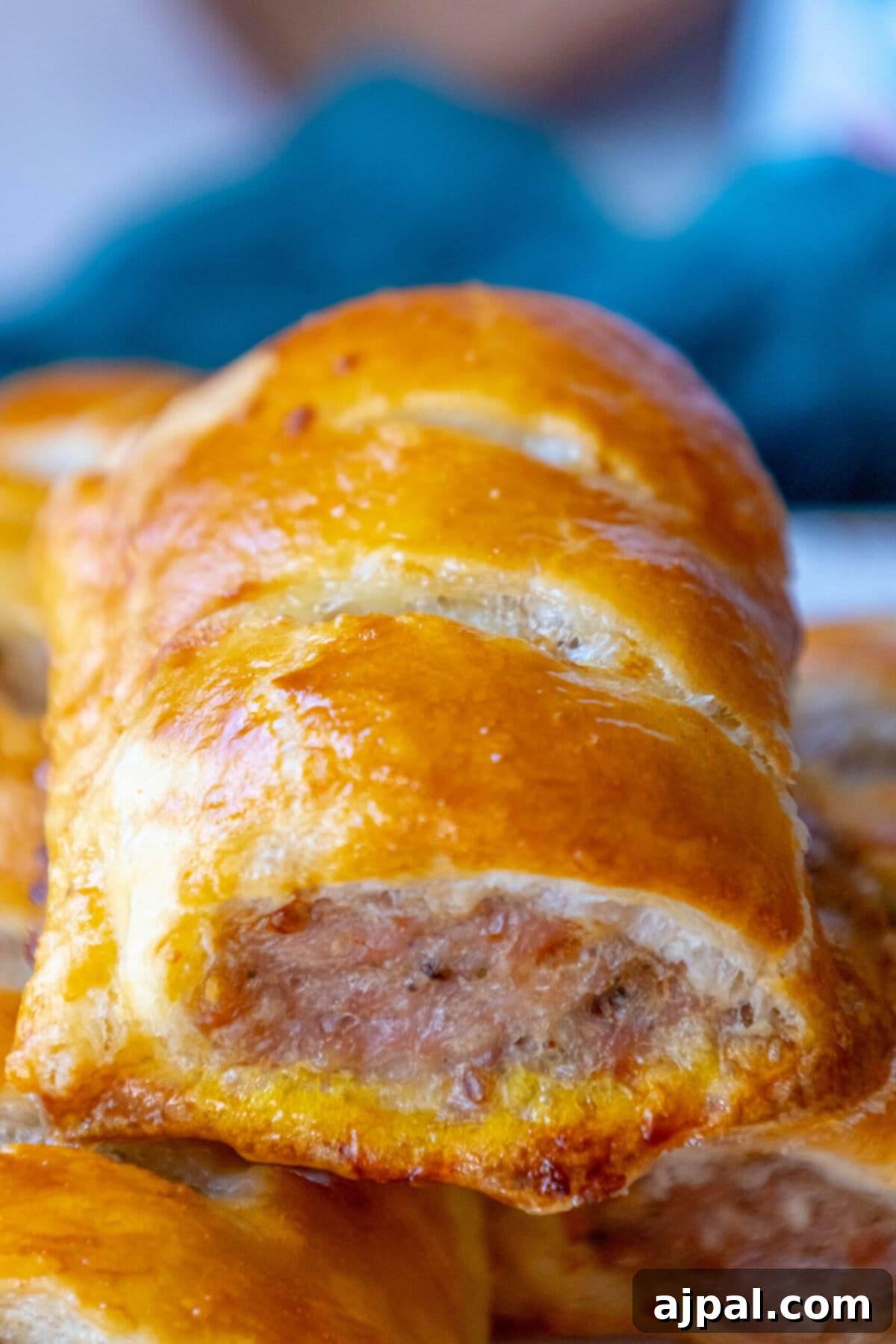 Classic English Sausage Rolls 11 Close-up of baked British sausage rolls with a blue kitchen towel in the background, highlighting their flaky crust.