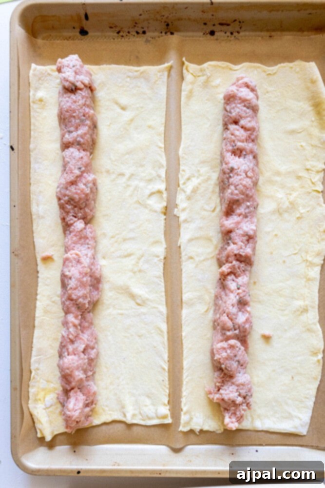 Classic English Sausage Rolls 7 Puff pastry dough laid out on parchment paper with a log of seasoned sausage meat placed down the center.