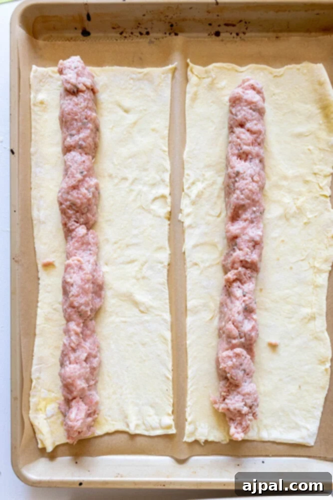 Classic English Sausage Rolls Recipe 7 Puff pastry dough laid out on parchment paper with a long roll of seasoned sausage meat placed down the center, ready to be folded.