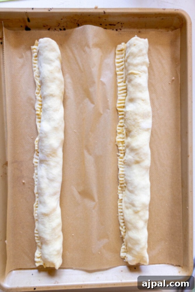 Classic English Sausage Rolls 8 Uncut long sausage rolls resting on parchment paper before baking.