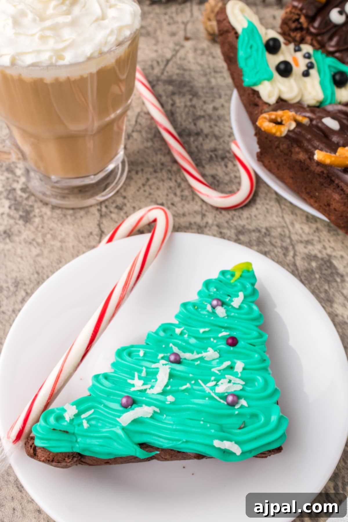 A festive plate showcasing frosted Christmas brownies in the shapes of snowmen, Christmas trees, and reindeer, alongside other holiday decorations.
