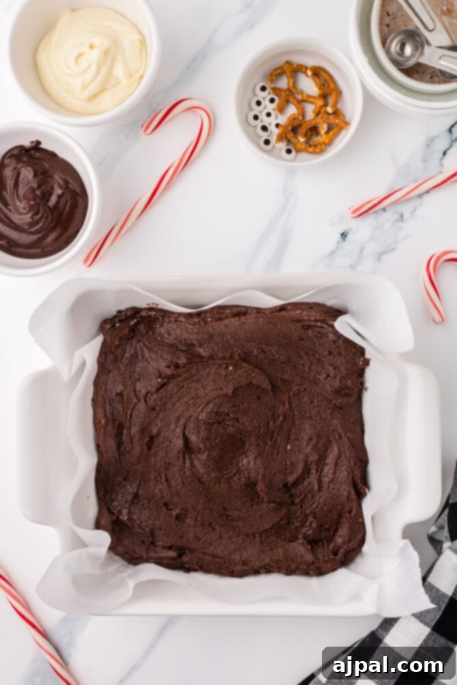 Brownie batter evenly spread in a baking dish lined with parchment paper, ready for the oven.
