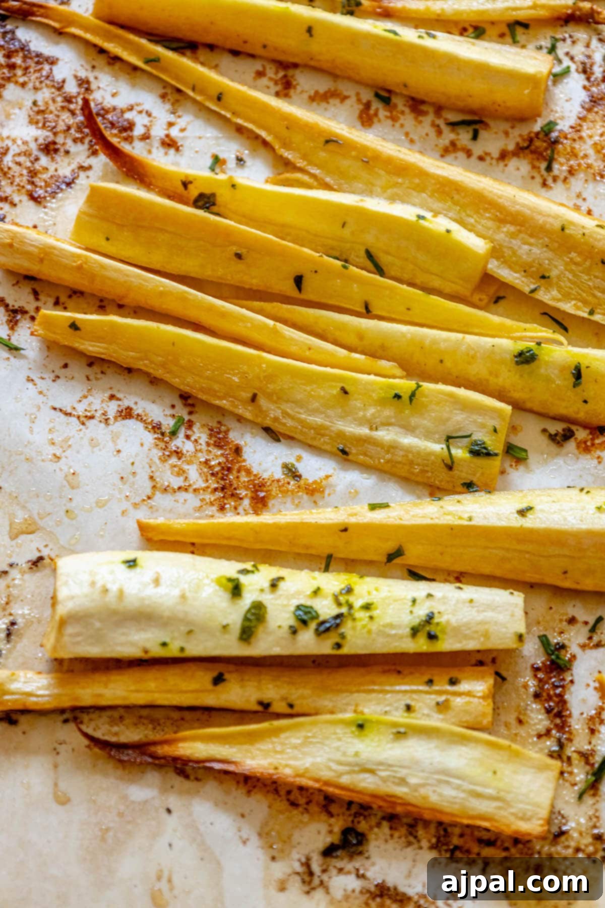 roasted parsnips seasoned with garlic butter and herbs on a baking sheet lined with parchment paper