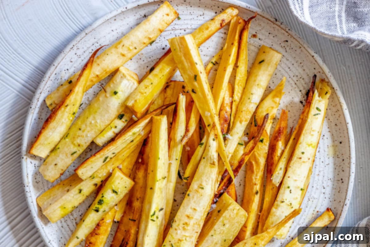 roasted parsnips seasoned with garlic butter and herbs on a white speckled plate next to a blue striped tea towel
