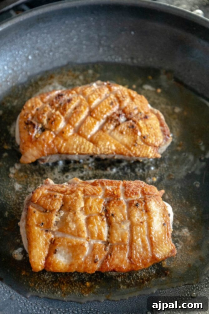 Golden-Crisp Duck Breast with Zesty Orange Reduction 5 Duck breast searing in a pan, with the fat rendering beautifully and the skin becoming golden brown and crispy.