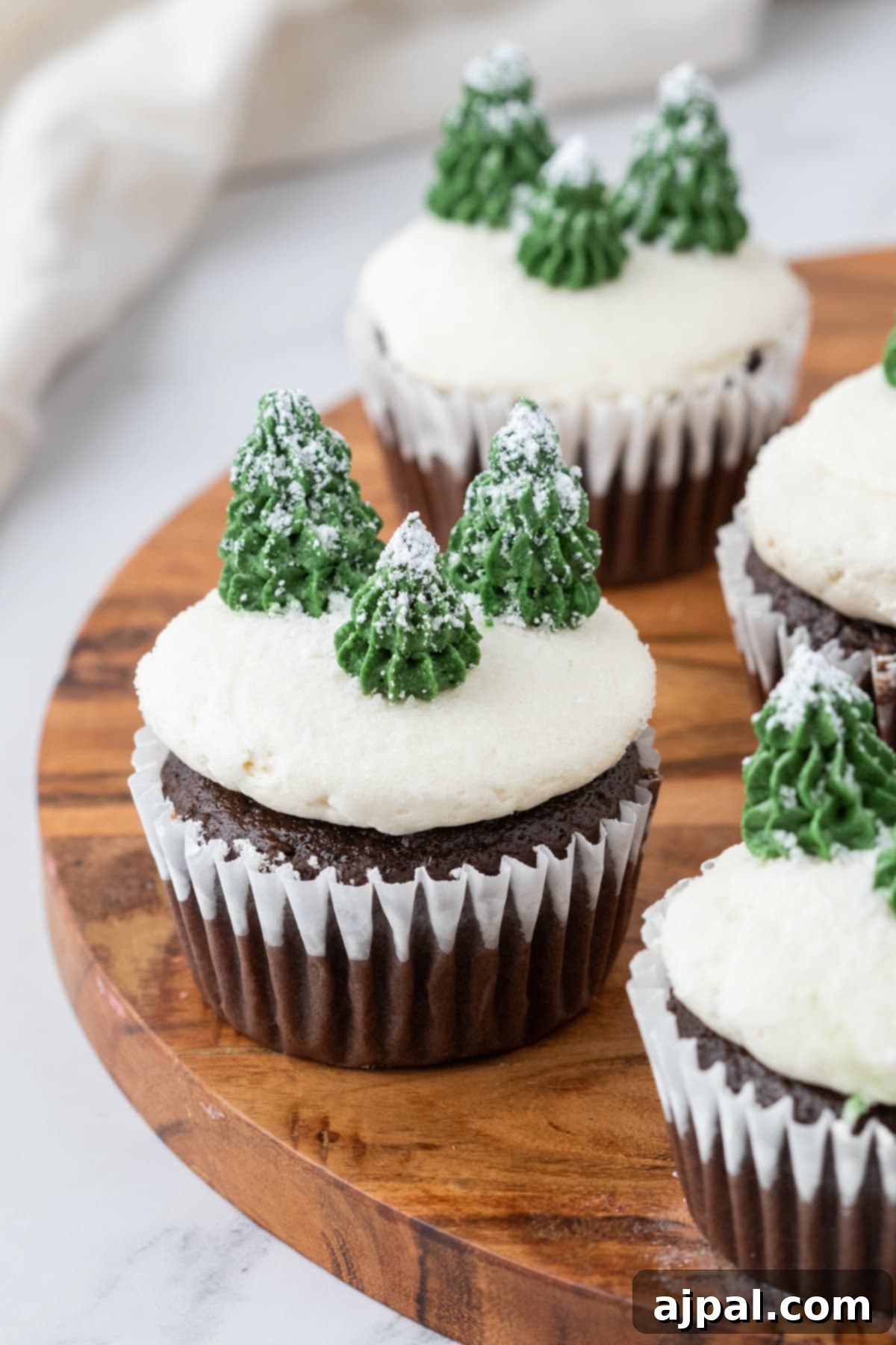 Delightful mint chocolate cupcake adorned with buttercream icing, powdered sugar 'snow,' and piped buttercream trees, resting on a pristine plate.
