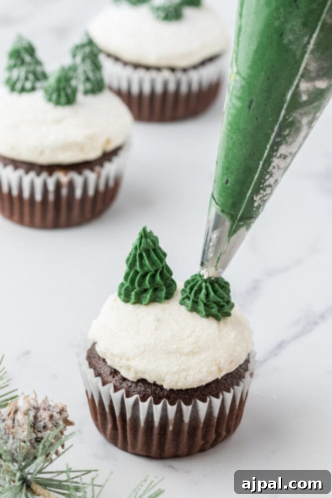 A skilled hand pipes a vibrant green Christmas tree onto a chocolate mint cupcake, using buttercream frosting and a star tip to create a festive, edible decoration.