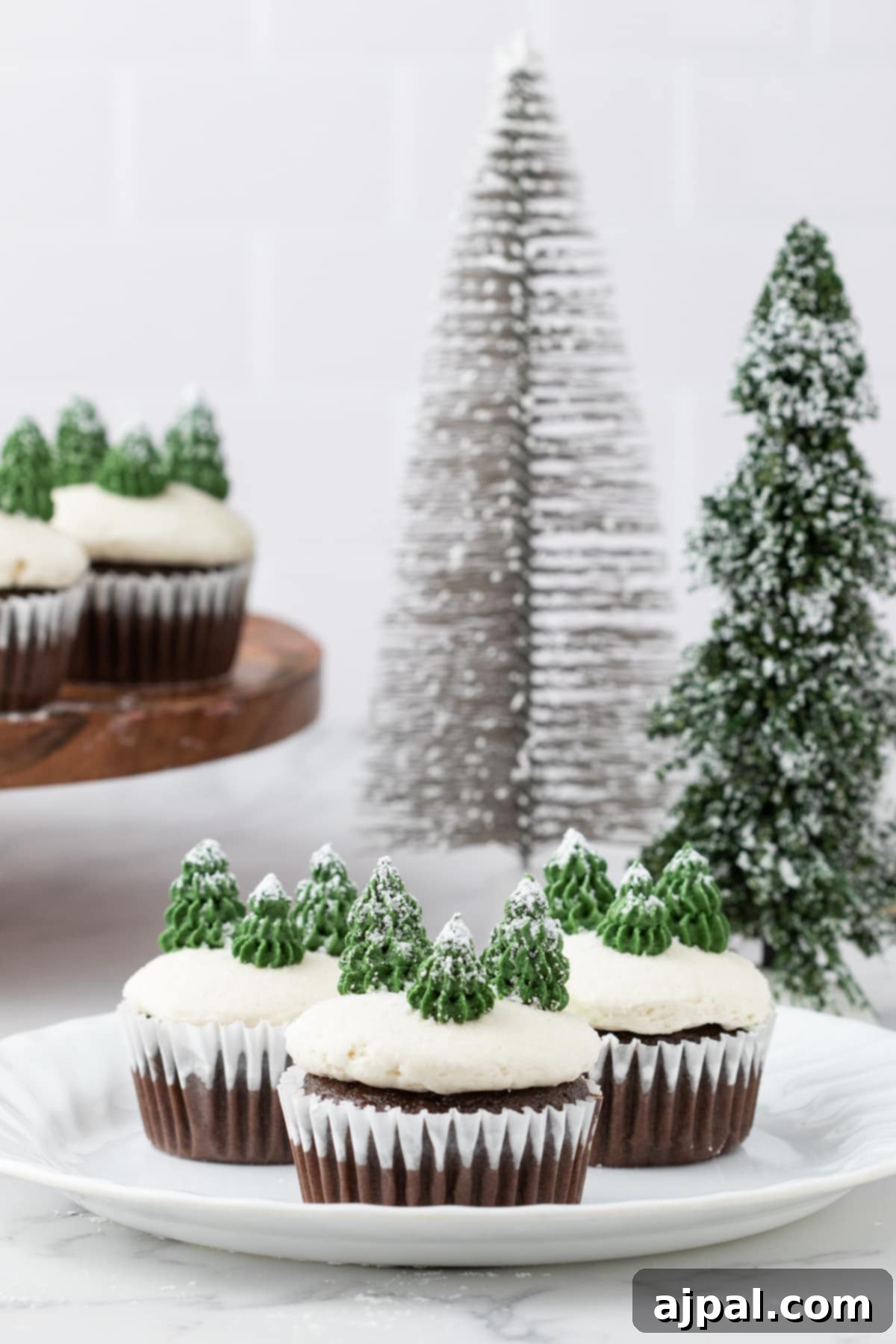 A charming plate of winter mint chip cupcakes, artfully decorated with festive Christmas trees and a dusting of powdered sugar snow, ready for holiday enjoyment.