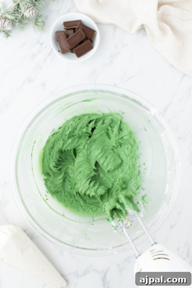 Lush green buttercream frosting, perfectly mixed, rests in a clear glass bowl on a elegant marble countertop, awaiting use.