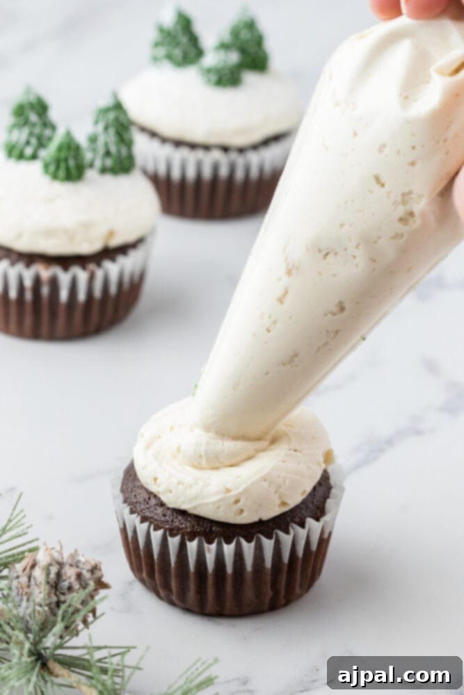 A skilled hand expertly pipes pristine white buttercream icing onto a moist chocolate mint cupcake, creating a smooth, inviting base for decoration.