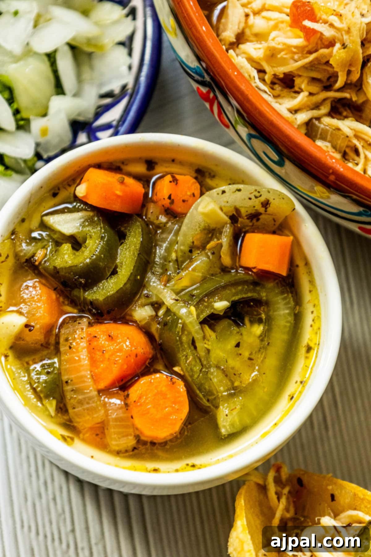 Zesty Carrot Jalapeno Relish 2 pickled carrots, onions, and jalapeno salsa in a white bowl on a table next to a bowl of chopped onions and a bowl of shredded chicken