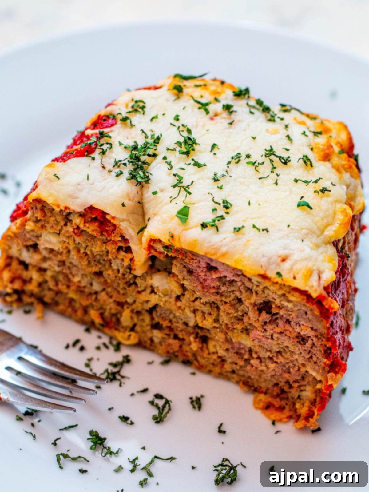 meatloaf covered in cheese and parsley on a white plate with a fork