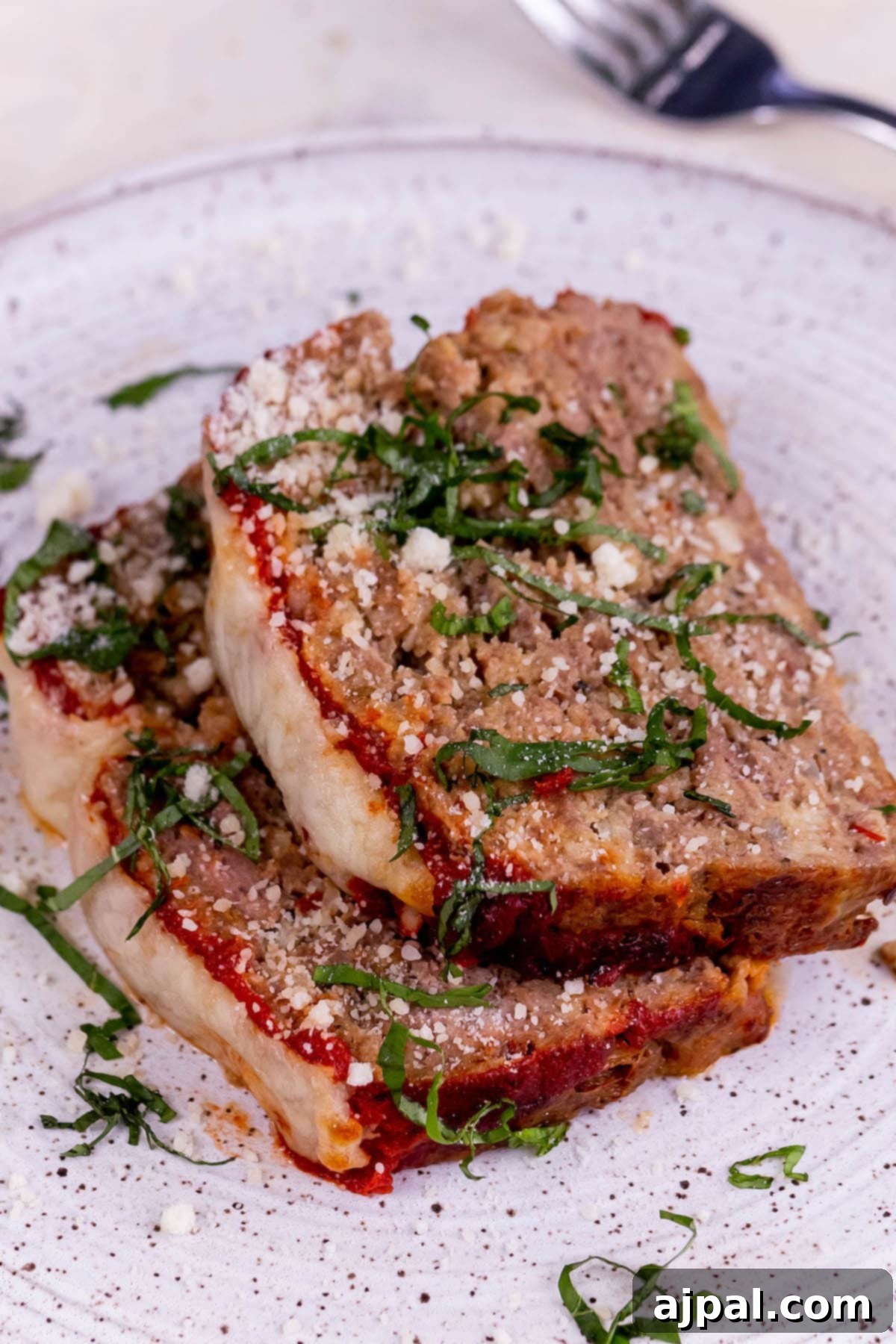slices of meatloaf baked with melted mozzarella cheese and tomato sauce on a plate with ribbons of basil on top 
