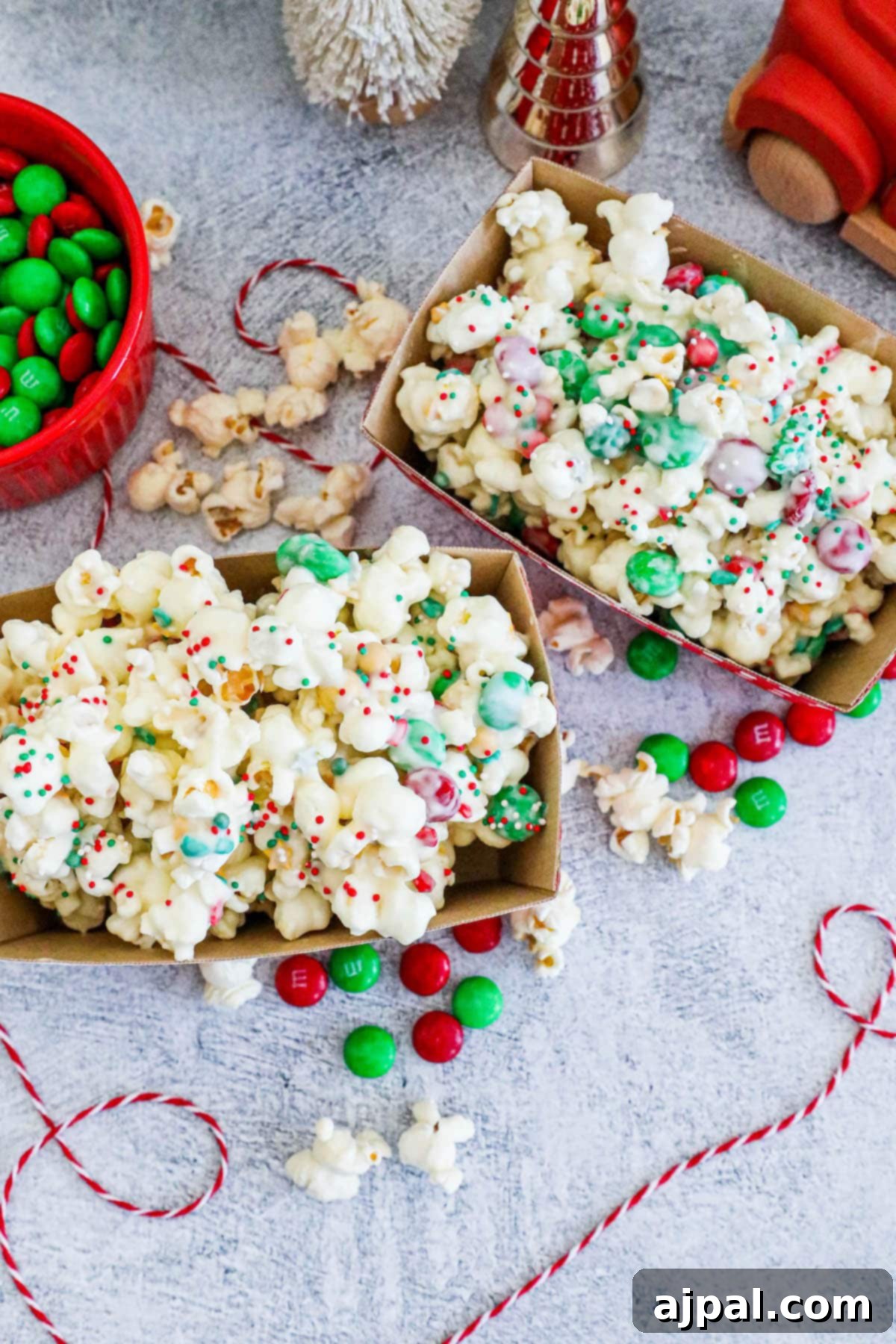 Two containers of popcorn, generously coated with white chocolate, festive sprinkles, and colorful candies.