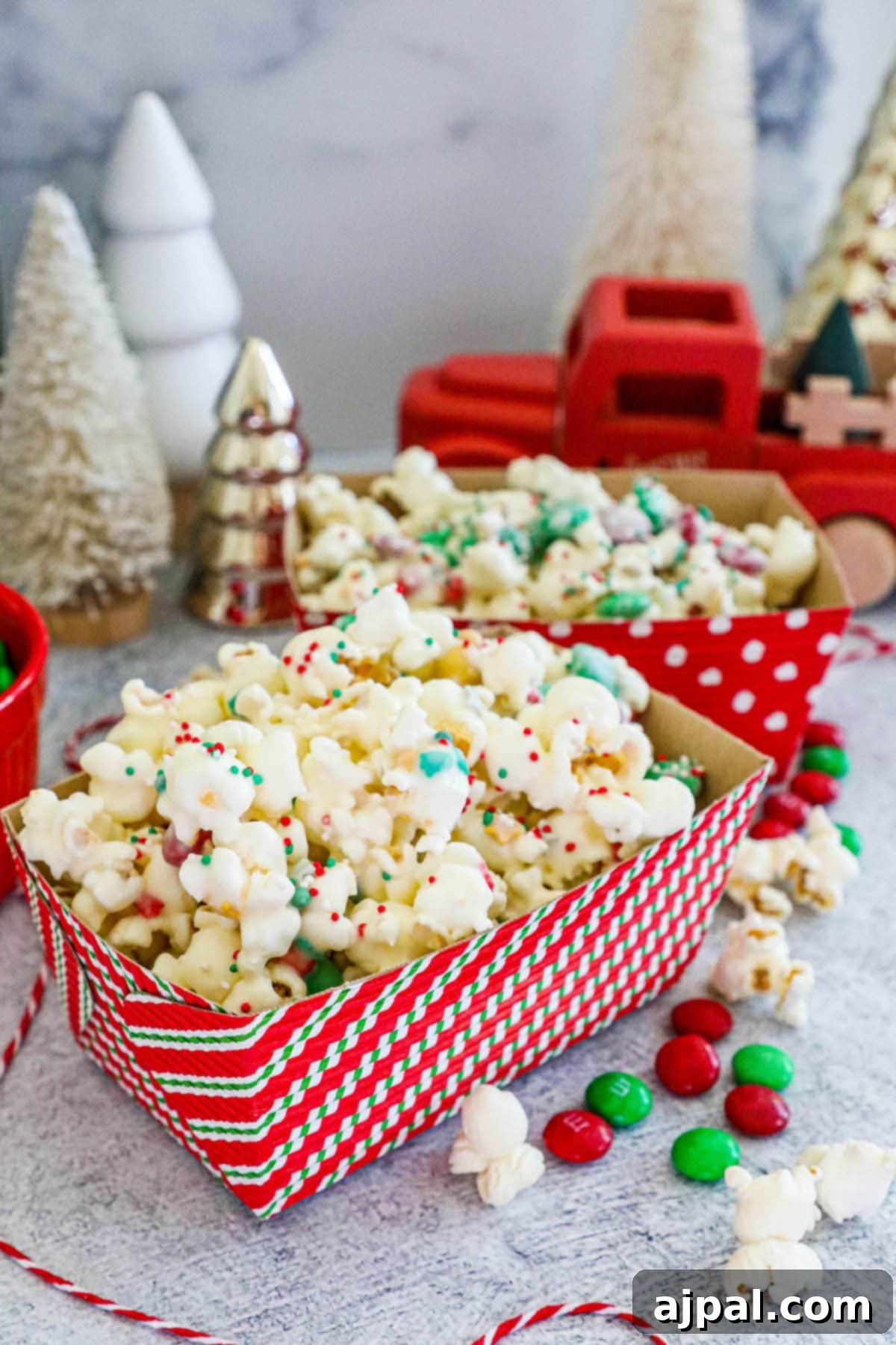A festive striped box filled with colorful reindeer popcorn, set against a charming background of twinkling Christmas trees.