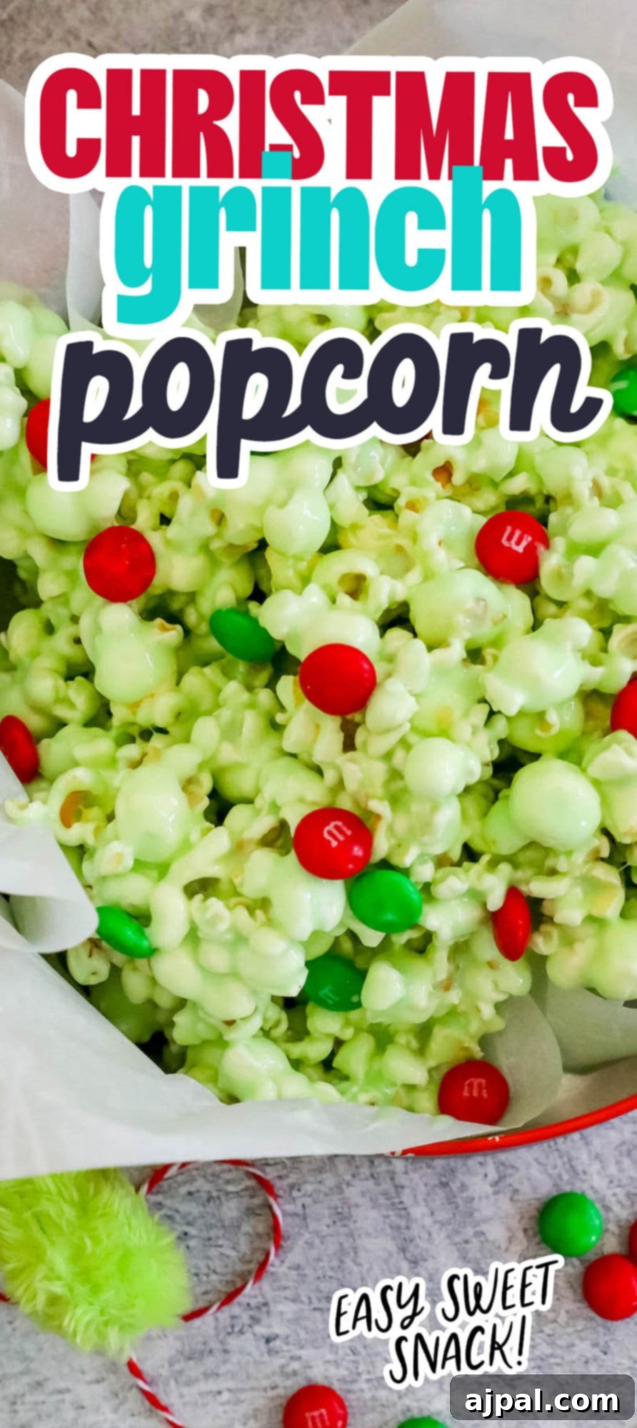 A bowl of green candy-coated popcorn with vibrant green and red Christmas candies and a festive ribbon.