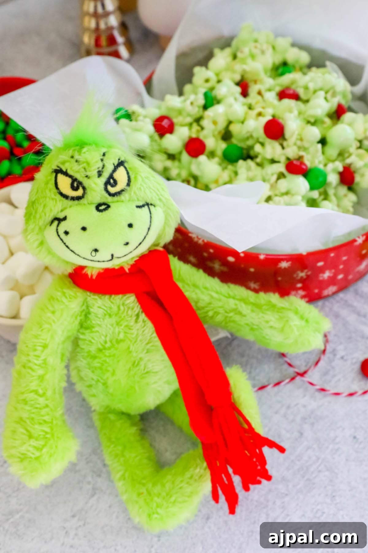 Grinch's Holiday Popcorn 4 a Grinch doll in front of a red bowl with Christmas candied popcorn colored green with green and red candy