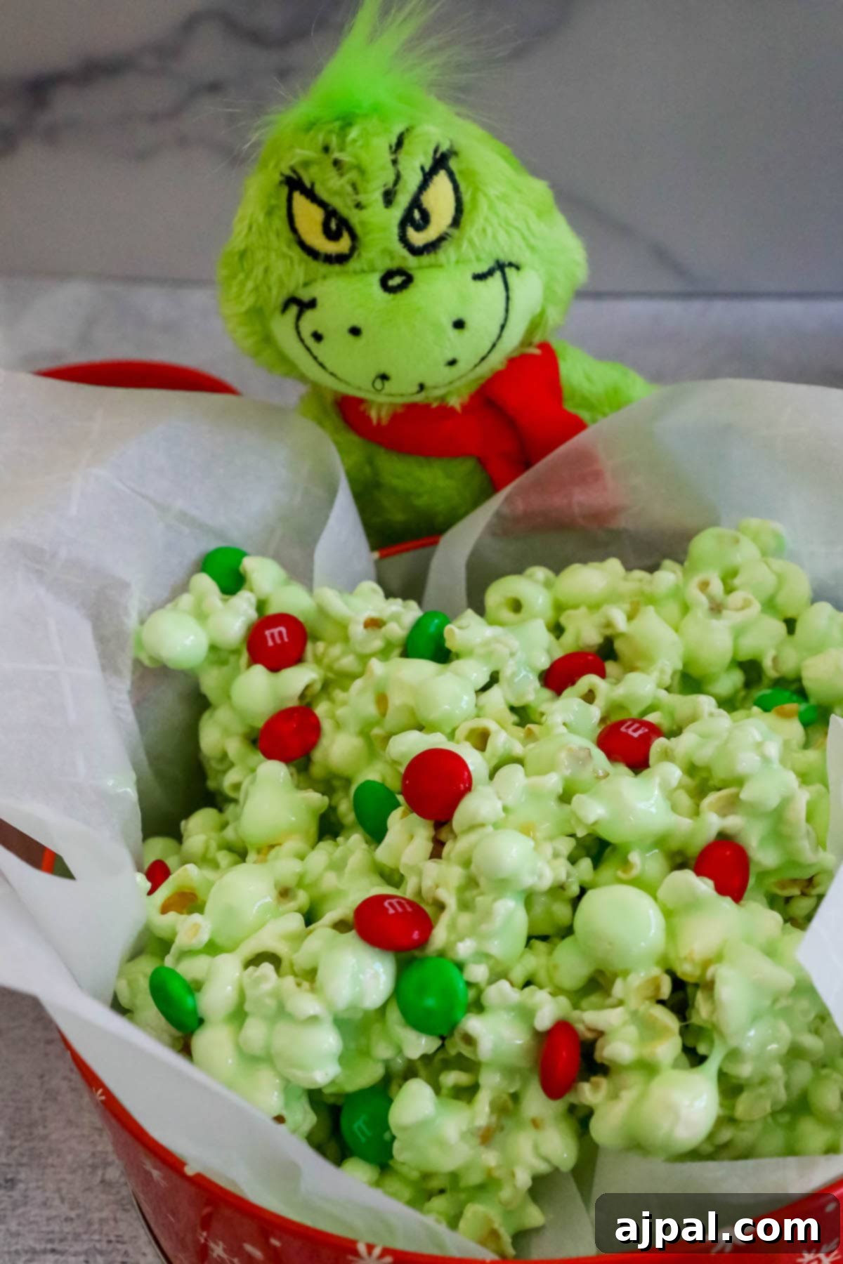 A bowl of green candy popcorn with red and green M&Ms and a cute Grinch doll, perfect for festive snacking.