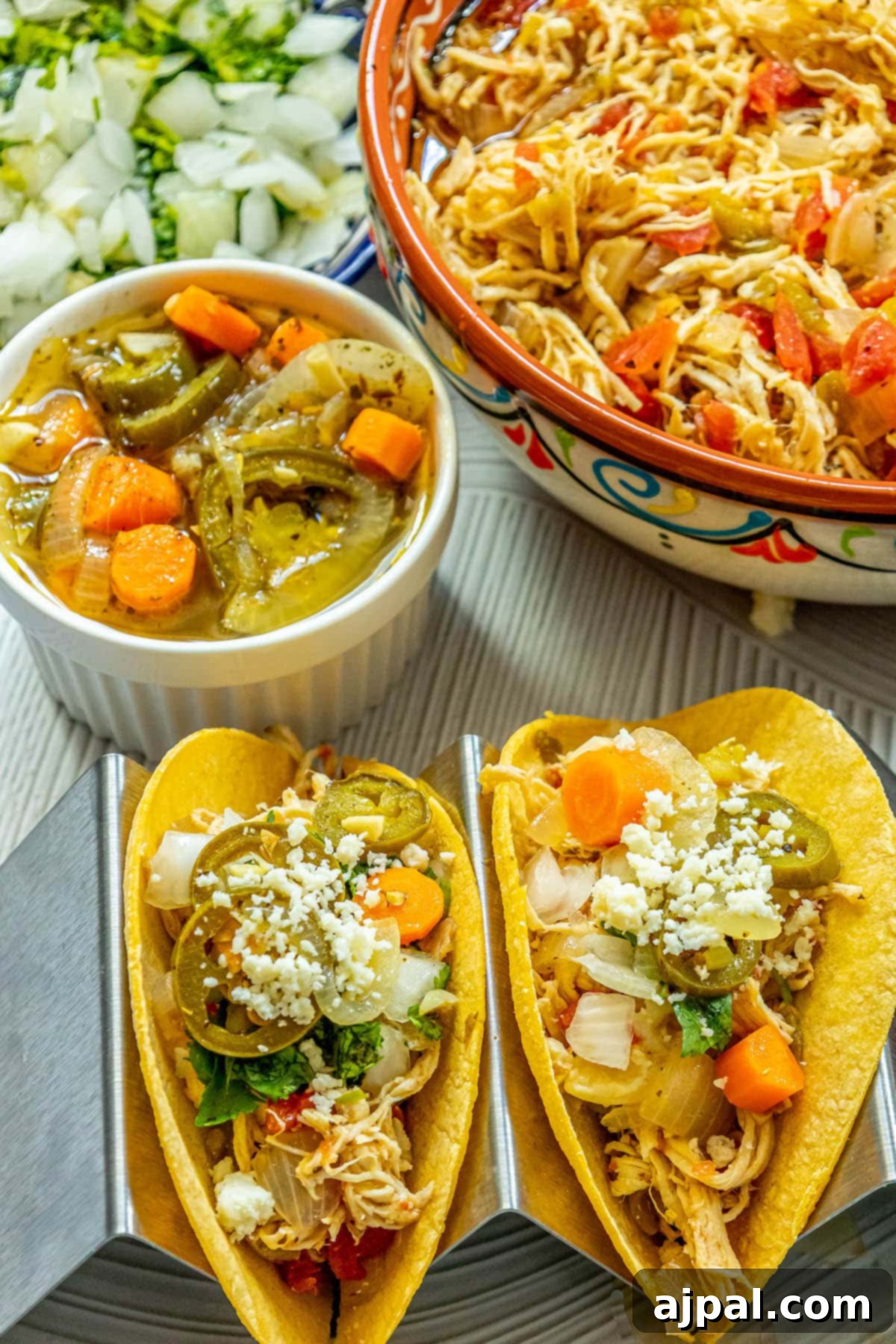 A close-up view of two delectable chicken tacos in a metal stand, filled with tender shredded chicken, tangy pickled jalapenos, rich crumbled white cheese, and fresh chopped cilantro. In the foreground, a vibrant bowl of pickled carrot and jalapeno salsa awaits as the perfect accompaniment.