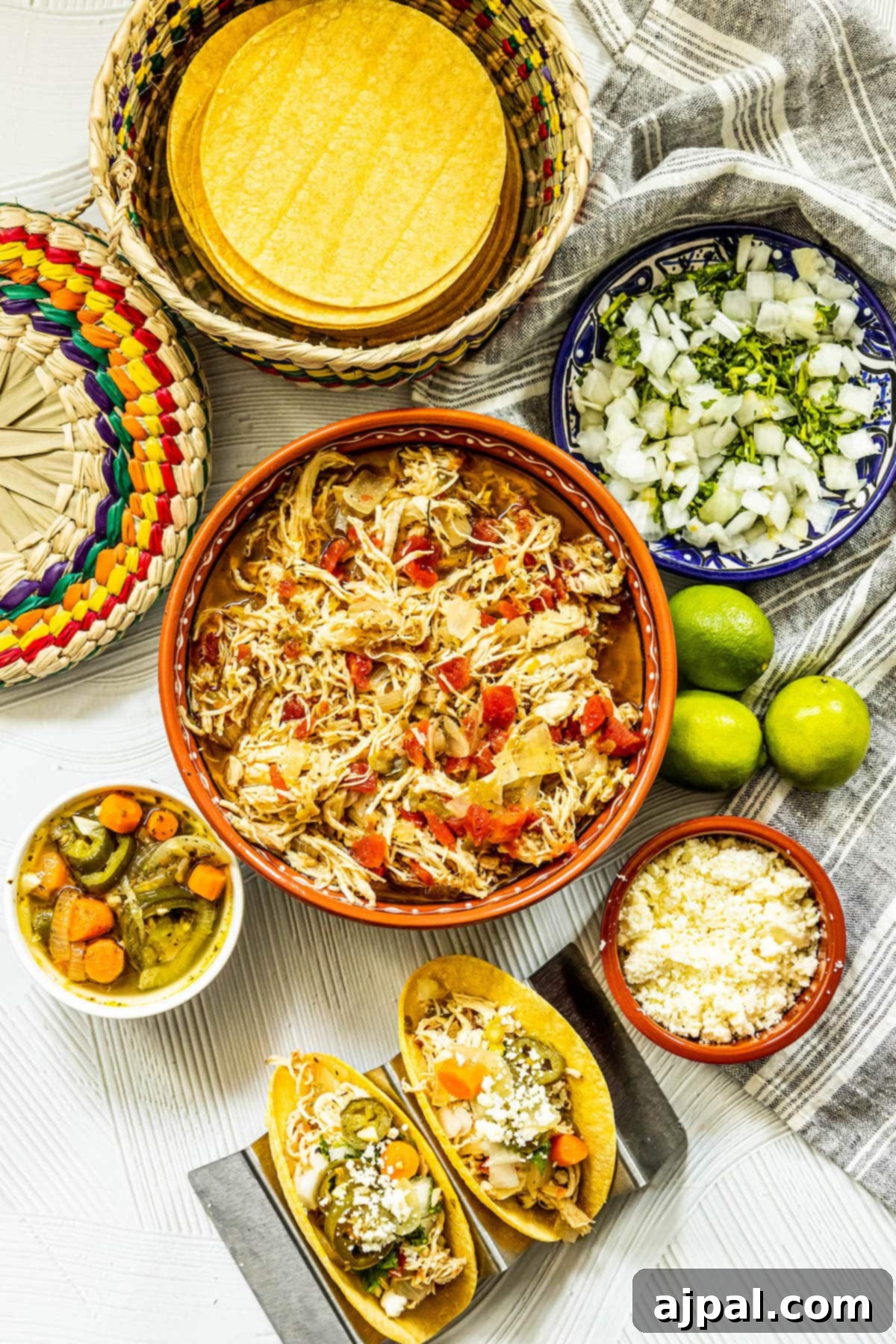 A vibrant and appetizing display of Mexican cuisine, featuring shredded green chile chicken tacos served in various bowls on a rustic wooden table, surrounded by an assortment of fresh toppings and condiments.