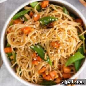 noodles with carrots, peas, peanuts, and chopsticks along the bowl.