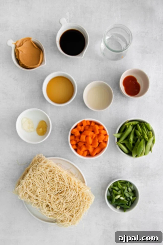 Kickin' Peanut Noodles 4 A colorful array of ingredients for spicy peanut noodles, including fresh carrots, snap peas, soy sauce, creamy peanut butter, uncooked noodles, and sesame oil, neatly arranged on a counter.