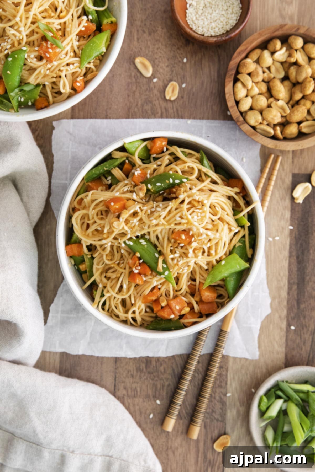 Close-up of peanut noodles with peas and carrots, ready to be served, tossed in sauce.