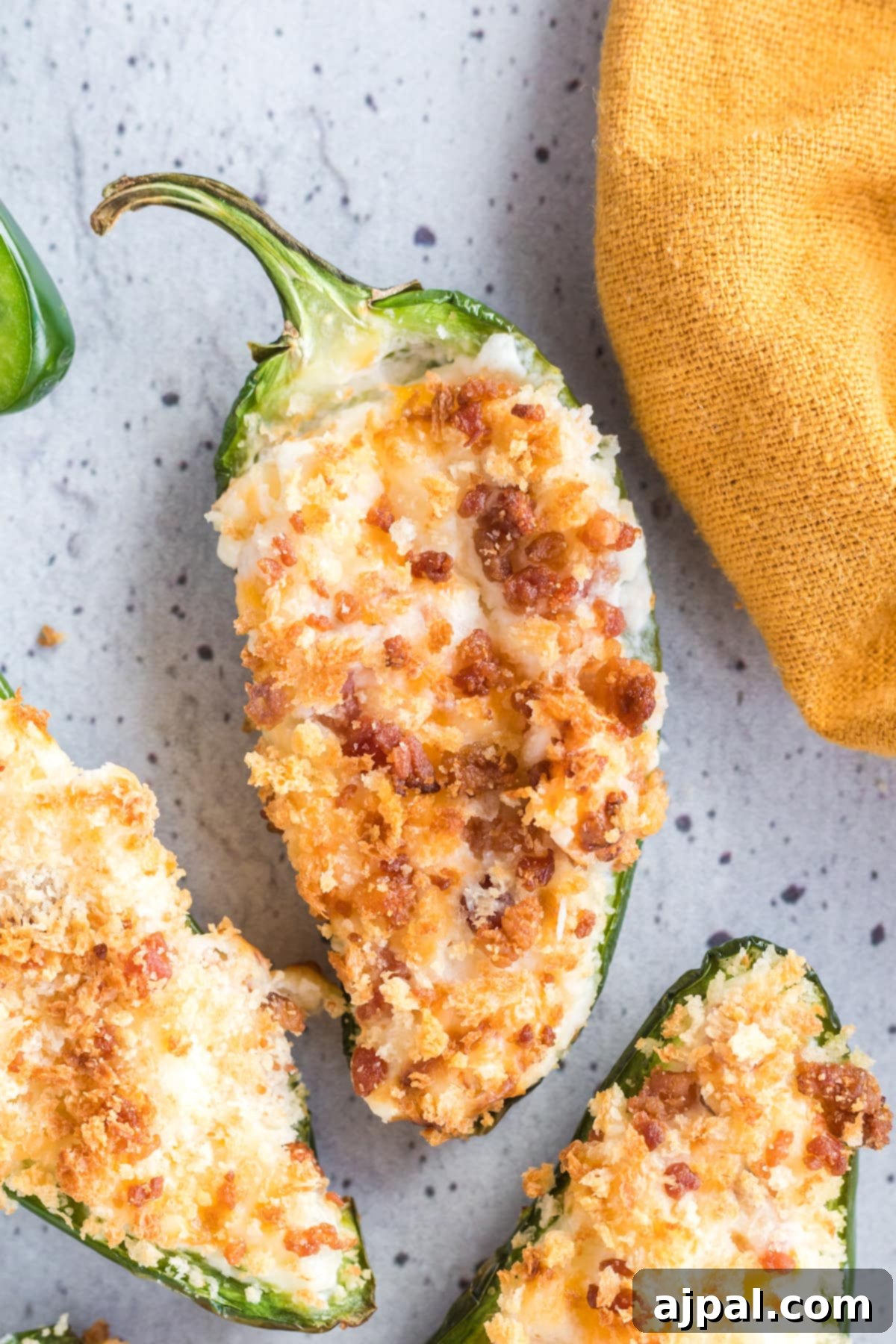 Air-fried jalapeño peppers sliced in half, generously stuffed with a creamy cheese mixture and golden-brown breadcrumbs, presented on a speckled plate.