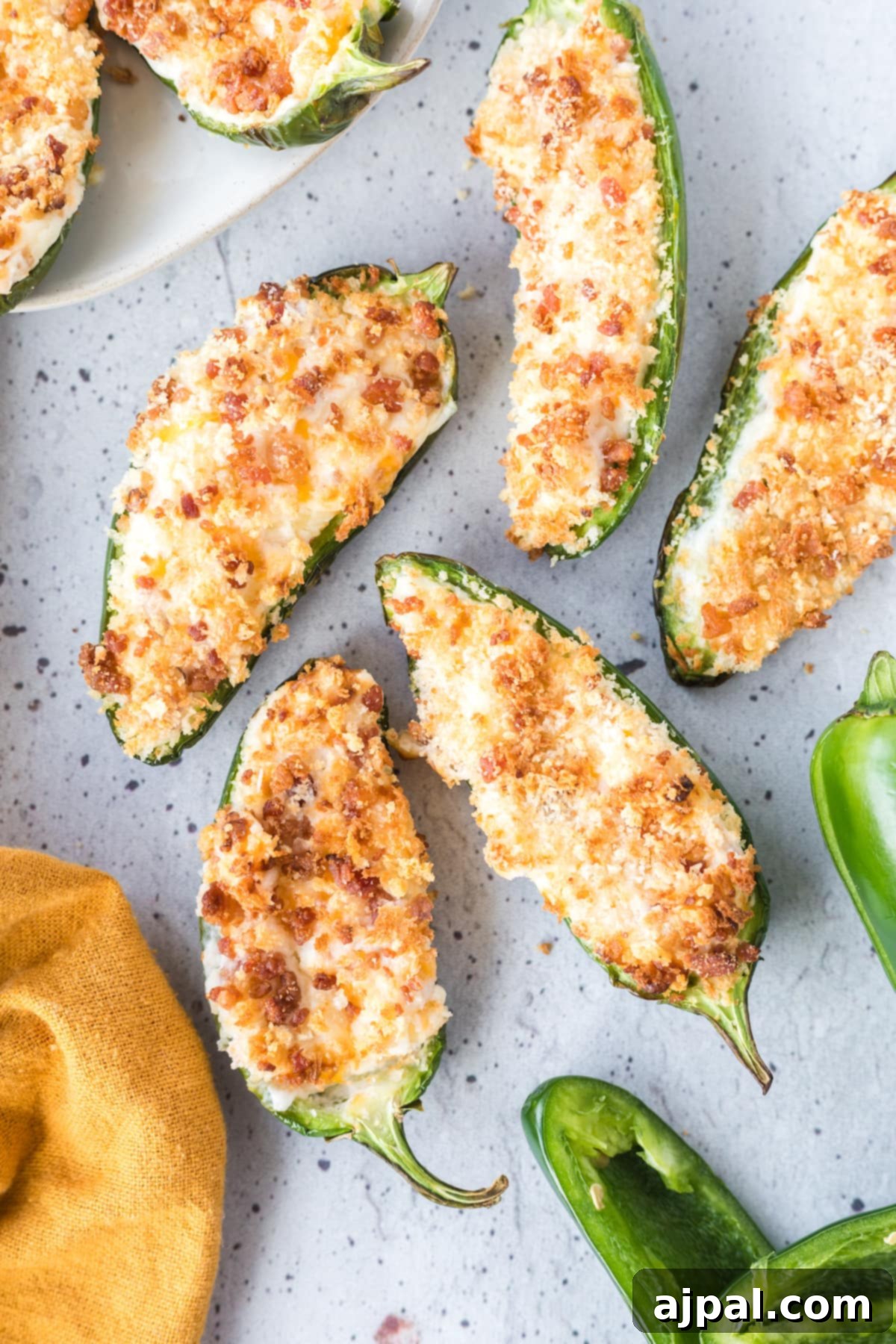 Air-fried jalapeño peppers, halved and stuffed with cream cheese and breadcrumbs, artfully arranged on a speckled plate alongside a vibrant yellow towel.