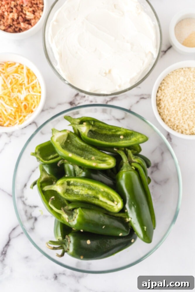 Fresh jalapeño peppers, sliced in half lengthwise and deseeded, ready for filling, arranged in a bowl next to other ingredient bowls.