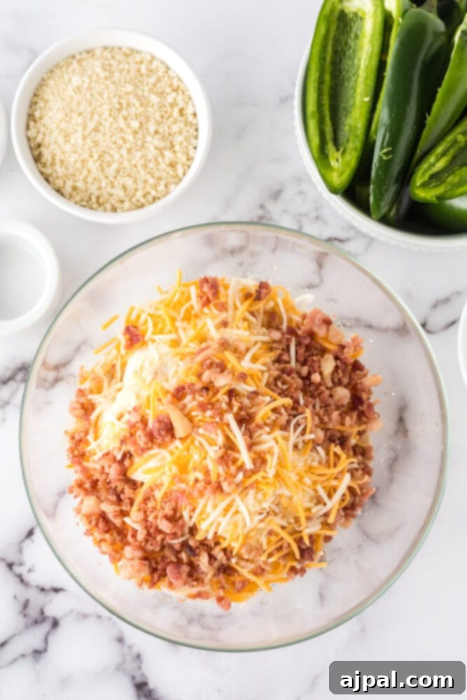 A glass bowl containing cream cheese, shredded Monterey Jack cheese, crumbled bacon, onion powder, and garlic salt, ready to be mixed for the popper filling.