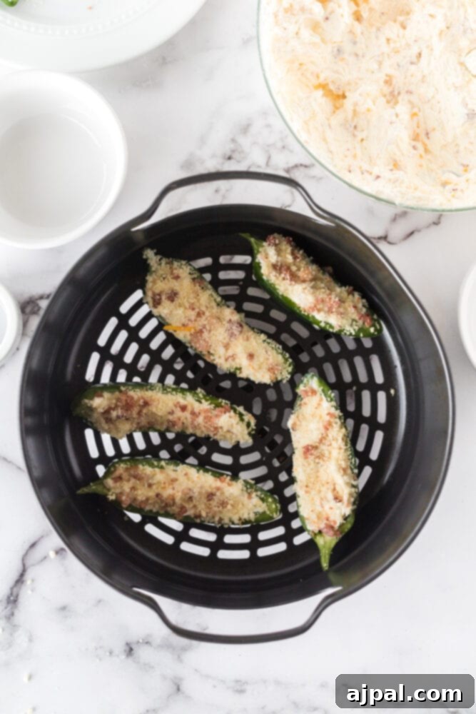 A raw jalapeño pepper half, filled with cream cheese mixture and topped with panko breadcrumbs, resting in the basket of an air fryer, ready for cooking.