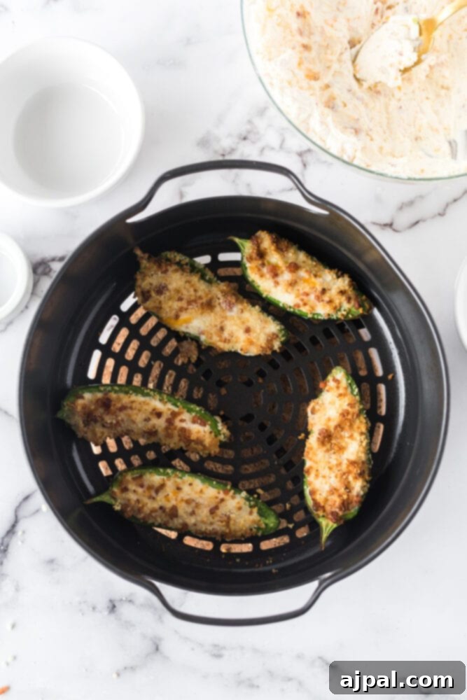 Golden-brown, perfectly air-fried jalapeño poppers, with their creamy filling and crispy panko topping, cooling in the air fryer basket after cooking.