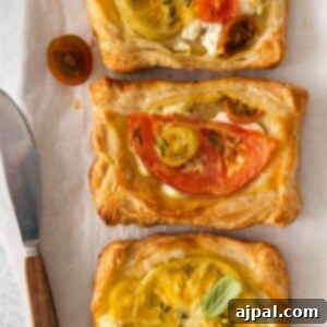 Two vibrant tomato and goat cheese tarts, perfectly baked and artfully arranged on parchment paper with fresh tomatoes scattered around, creating an inviting visual.