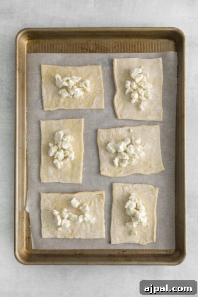 Tomato Goat Cheese Tarts 6 Goat cheese evenly spread across six puff pastry rectangles on a baking sheet, forming a creamy base for the tomatoes.