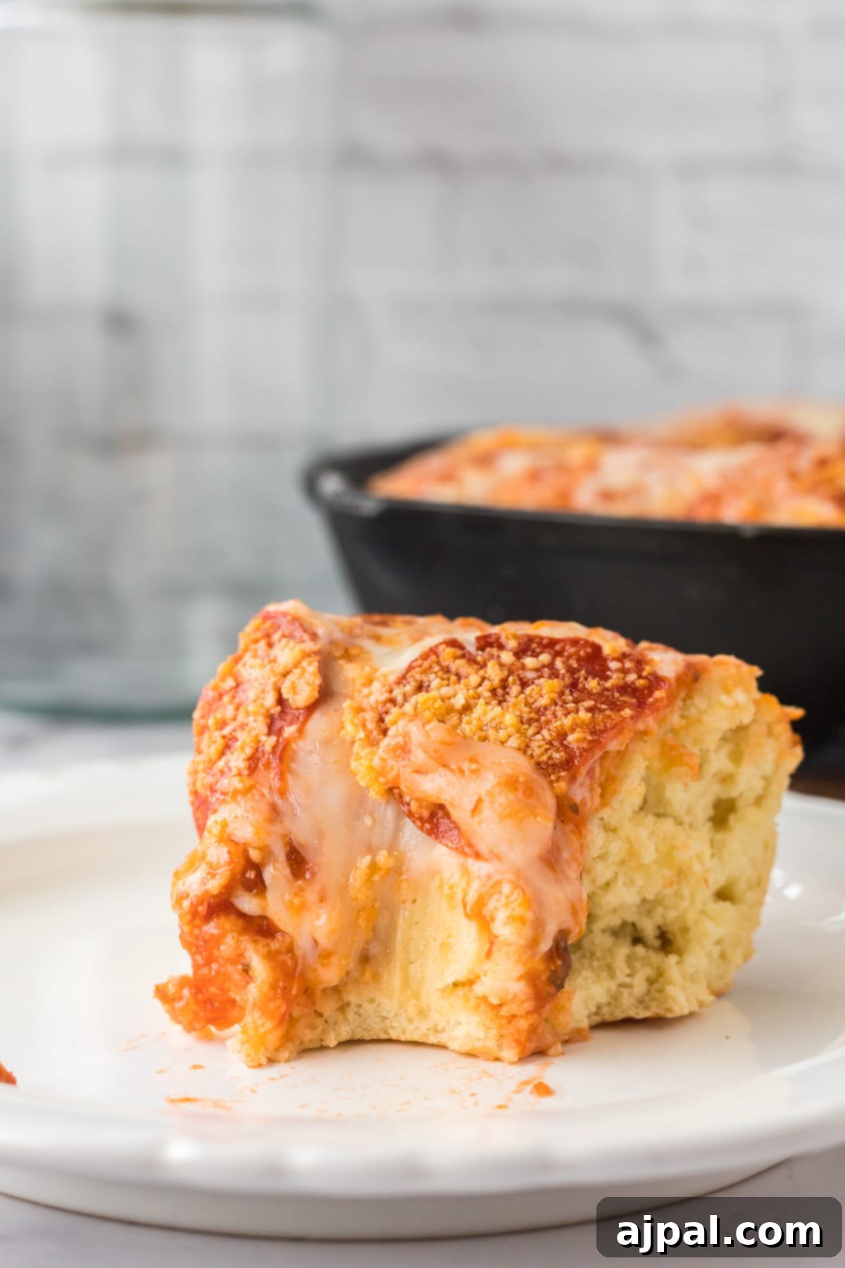 A perfectly baked slice of deep dish pizza on a plate with a bite taken out of it, showcasing its thick crust and generous fillings.