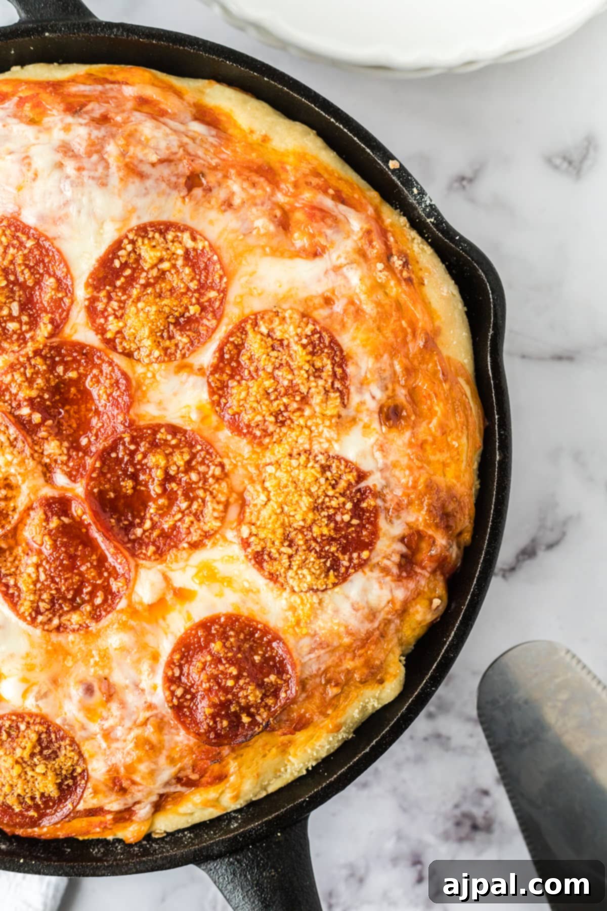 A golden-brown baked deep dish pizza in a cast iron skillet, generously sprinkled with parmesan cheese, ready to be served.