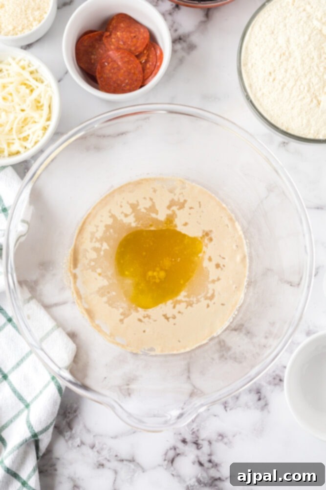 A bowl on a table containing olive oil, yeast, and warm water, beginning the proofing process for pizza dough.