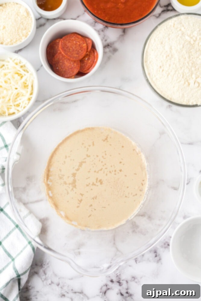 A close-up shot of proofed yeast in a mixing bowl on a table, showing a foamy and active surface.