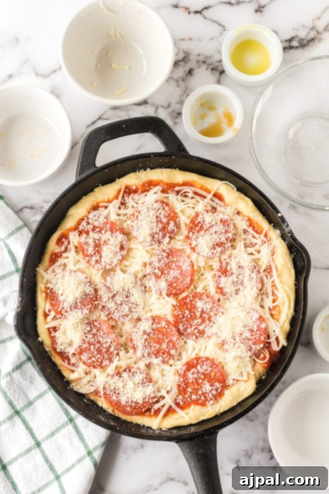 An unbaked deep dish pizza, assembled with its crust, sauce, and toppings, resting in a cast iron skillet on a table.