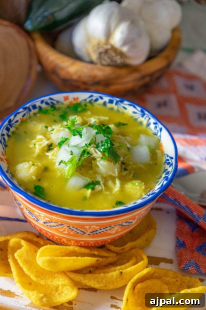 Zesty Green Chicken Posole 3 A bowl of easy chicken posole verde with a side of crispy tortilla chips on a rustic wooden table.