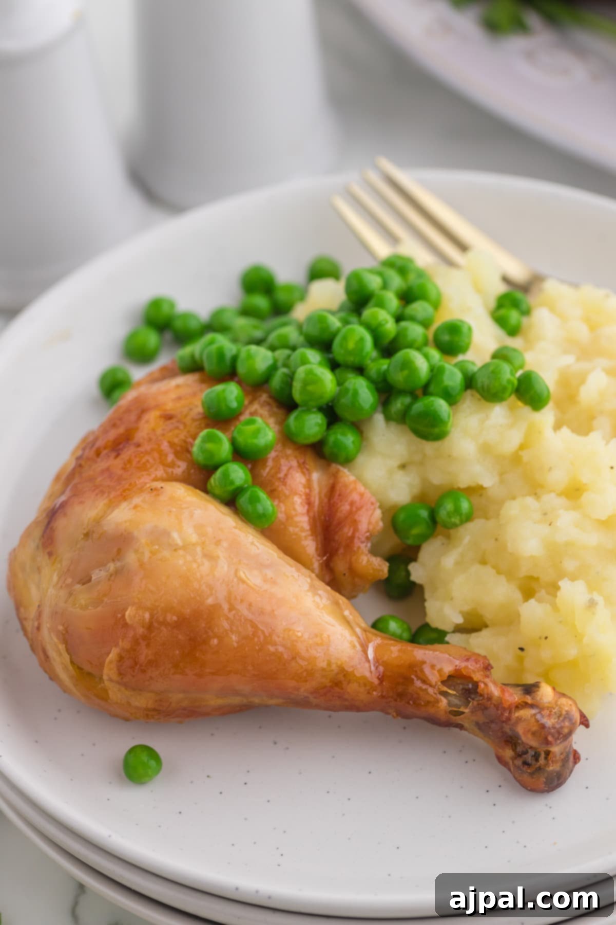 Roasted chicken leg on a white plate with peas and mashed potatoes, showcasing a comforting and complete Instant Pot meal.