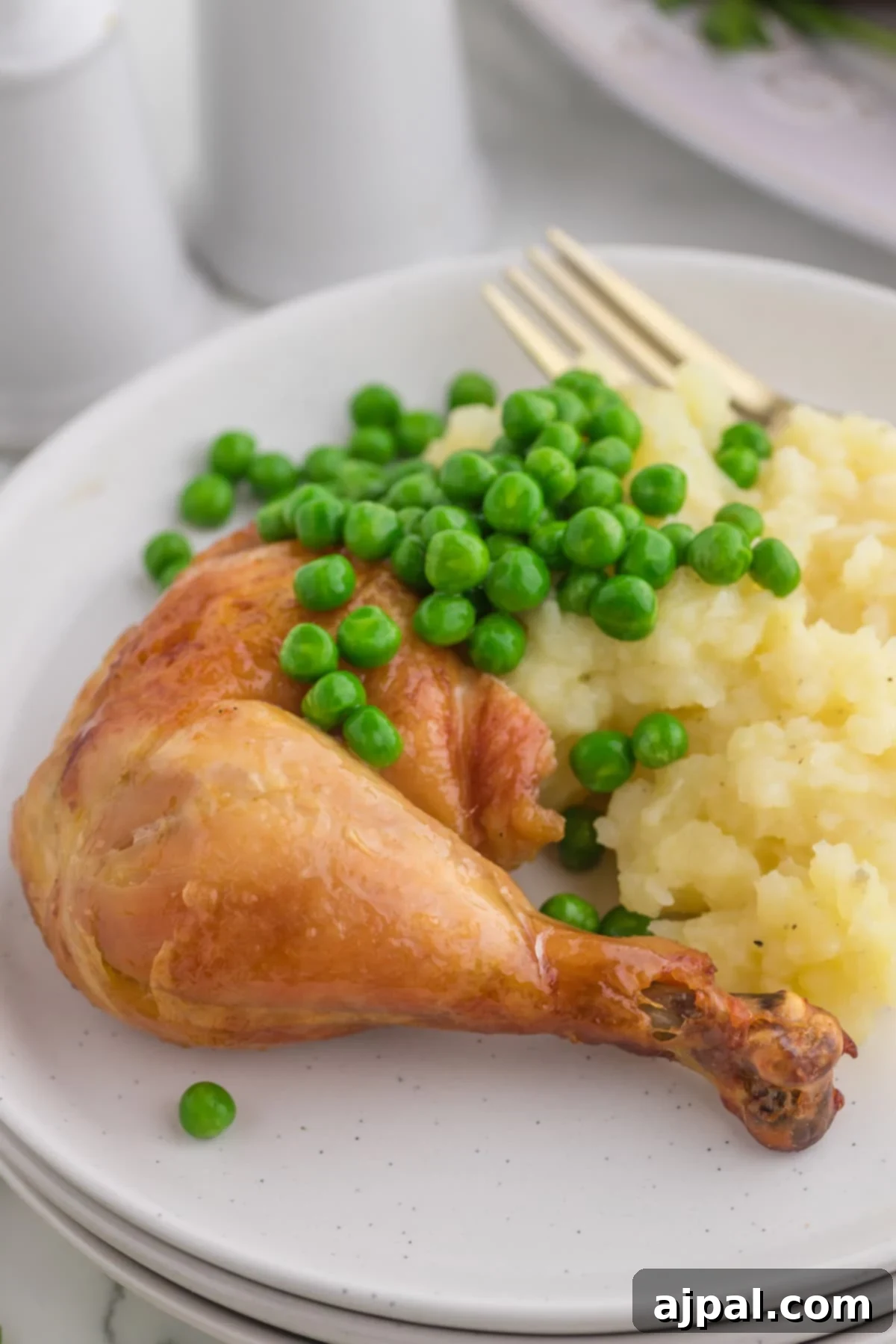 Perfect Instant Pot Whole Chicken 11 roasted chicken leg on a white plate with peas and mashed potatoes in front of an instant pot