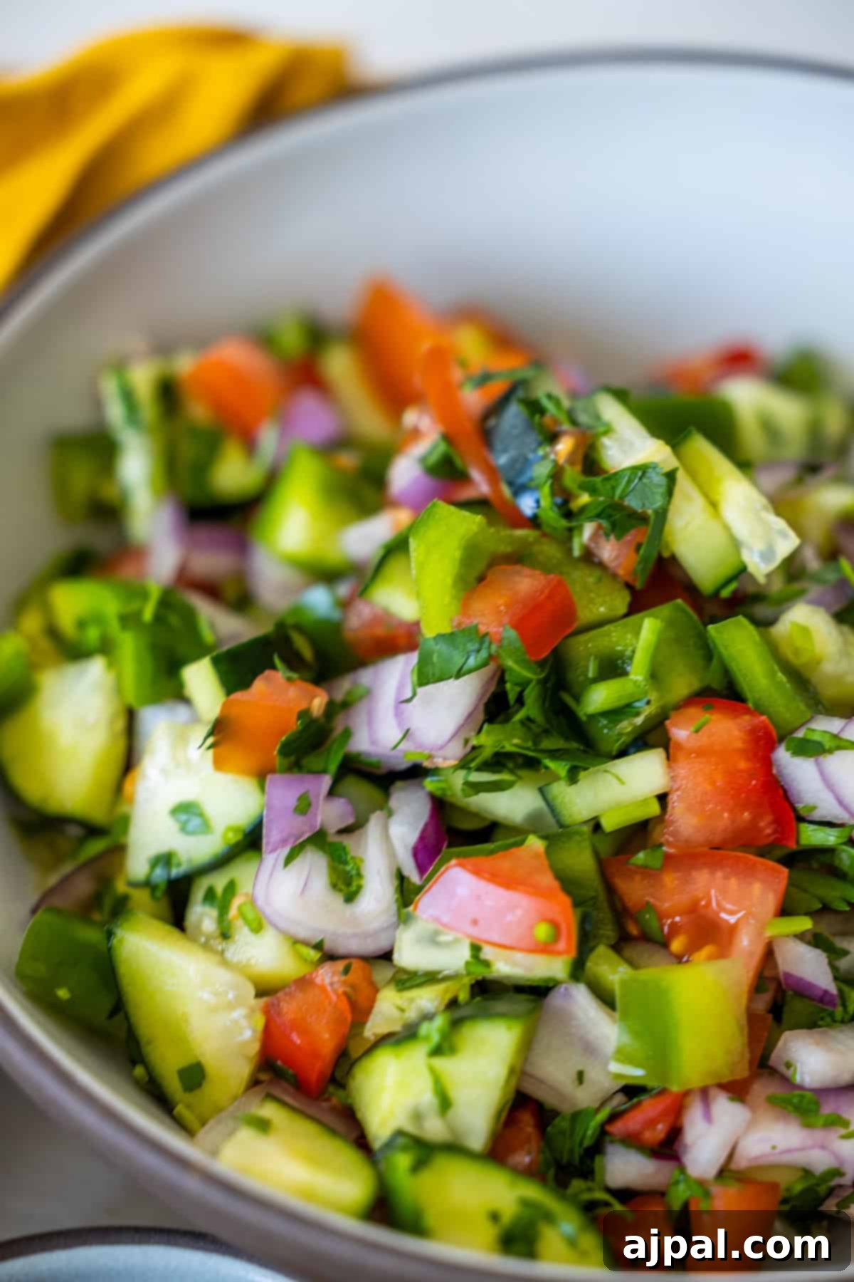 Authentic Jerusalem Salad 2 A vibrant bowl of freshly chopped Israeli salad featuring diced cucumbers, ripe red tomatoes, thinly sliced red onions, and bright green bell peppers, all beautifully garnished with fresh parsley.