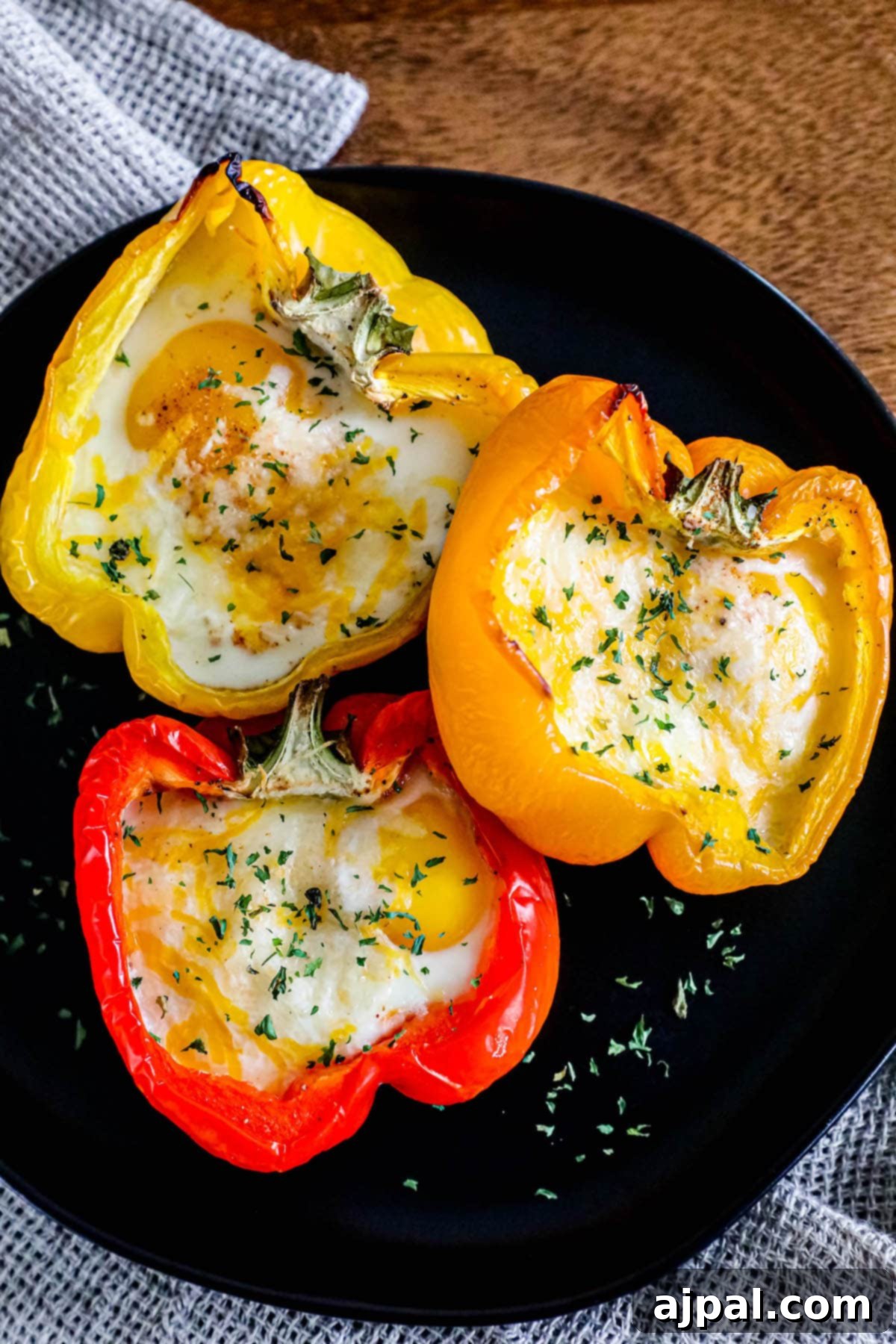 Bell Pepper Egg Bake 3 baked eggs inside half of a bell pepper with melted cheese and herbs on top on a black plate