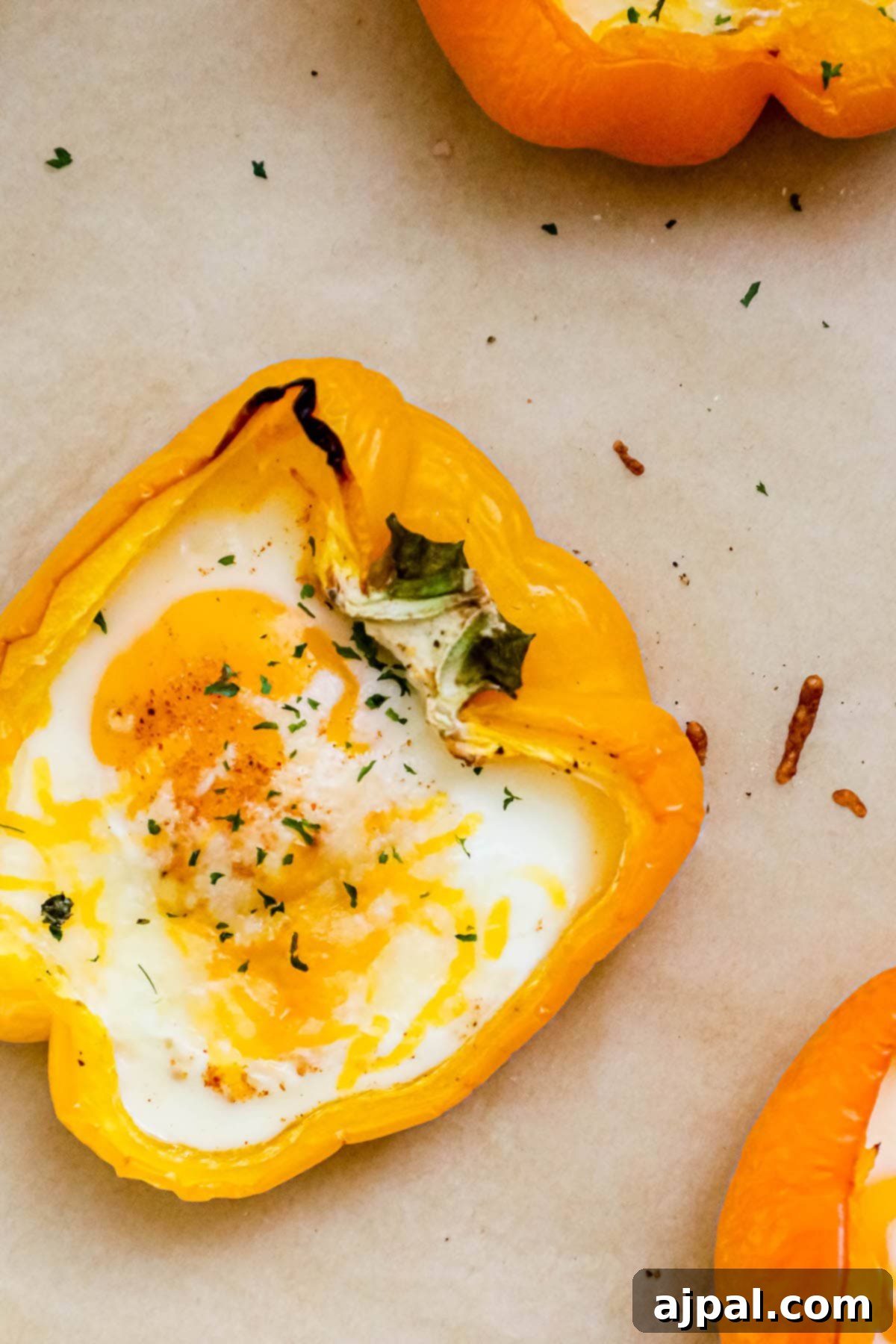 Bell Pepper Egg Bake 8 baked eggs inside half of a bell pepper with melted cheese and herbs on top on a baking sheet with parchment paper
