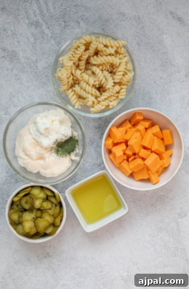 Tangy Dill Pasta Delight 4 Individual bowls of pickles, mayonnaise, cheese, oil, pasta, and herbs laid out on a table, ready for preparation.