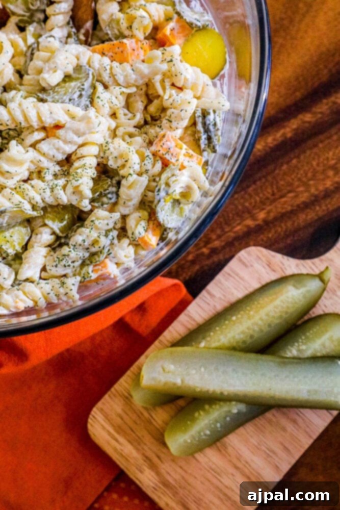 Tangy Dill Pasta Delight 5 A glass bowl filled with mixed pasta salad, featuring generous amounts of cheese and pickles, tossed in a creamy dill dressing.